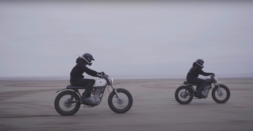 Zwei Männer fahren mit einem Yamaha SR 500-Motorrad am Strand