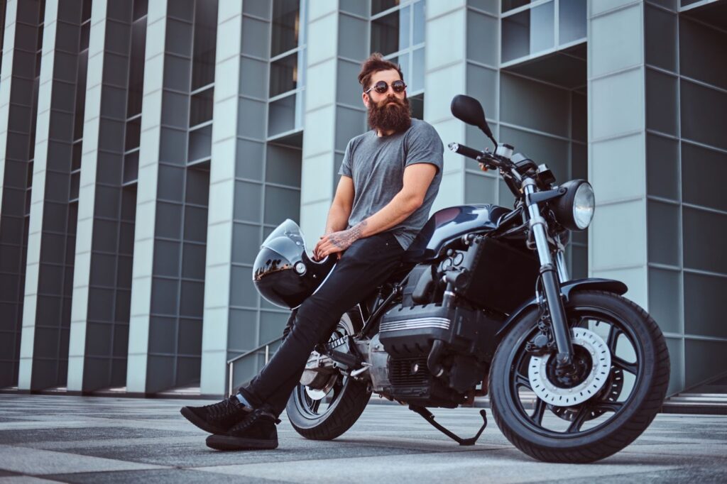 Ein bärtiger Mann hält einen Helm, während er auf seinem Motorrad sitzt